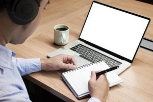 Businessman hand holding a pen to paperwork with white screen background mock up on display laptop with clipping path photo