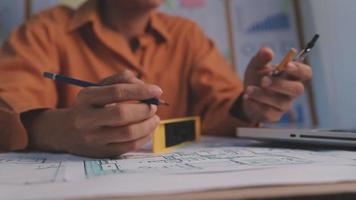 Dos colegas discutiendo el trabajo de datos y una tableta, un portátil con un proyecto arquitectónico en el sitio de construcción en un escritorio en la oficina video