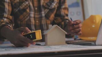 Dos colegas discutiendo el trabajo de datos y una tableta, un portátil con un proyecto arquitectónico en el sitio de construcción en un escritorio en la oficina video