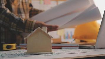 Dos colegas discutiendo el trabajo de datos y una tableta, un portátil con un proyecto arquitectónico en el sitio de construcción en un escritorio en la oficina video