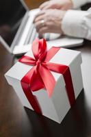 White Gift Box with Red Bow Near Man using Laptop photo