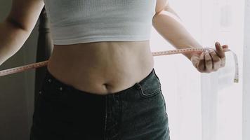 hermosa mujer gorda con cinta métrica usa su mano para exprimir el exceso de grasa que está aislado en un fondo blanco. ella quiere perder peso, el concepto de cirugía y descomponer grasa bajo el video