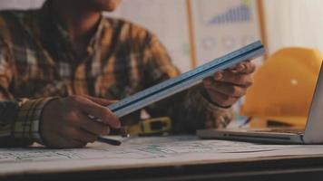 Dos colegas discutiendo el trabajo de datos y una tableta, un portátil con un proyecto arquitectónico en el sitio de construcción en un escritorio en la oficina video