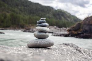 una pirámide de piedras desnudas apiladas una encima de la otra. piedras apiladas en forma de pirámide en la orilla del río contra el fondo de las montañas como equilibrio y equilibrio en la naturaleza, zen, budismo. foto