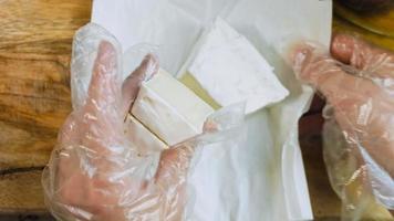 Der Koch schneidet Brie-Käse. Dekorationen aus Lebensmittelpapier im Hintergrund video