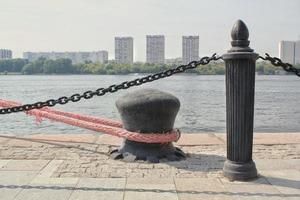 Steel metal parking bollard for ships with pink nautical mooring secured rope on a pier in port. Harbor sailing wharf quay. Marine water sea navigation transportation. Place for fixing boat and yacht photo