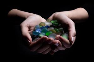 manos con piedras de colores, una mujer joven sostiene una colección de varias piedras preciosas minerales en bruto en su palma aisladas en negro foto