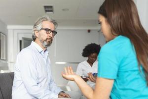 Young female doctor and senior man communicating in a waiting room at hospital. medicine, healthcare and people concept - doctor and patient meeting at hospital photo