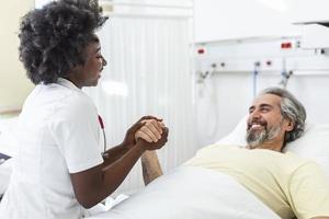 médico profesional que consulta y reconforta a un paciente anciano en la cama de un hospital o asesora en el diagnóstico de salud. médico o enfermera sosteniendo las manos del paciente mayor y consolándolo foto