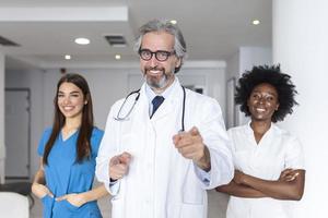 Closeup front view of group of mixed age doctors and nurses standing side by side and looking at the camera. Mature man doctor is in the front photo