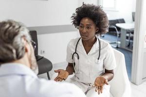 Black female doctor and senior man communicating in a waiting room at hospital. medicine, healthcare and people concept - doctor and patient meeting at hospital photo