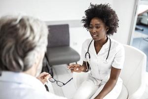 African American doctor consoling her mature patient in waiting room at medical clinic. photo