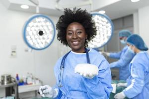 African American Plastic surgeon woman holding silicon breast implants in surgery room interior. Cosmetic surgery concept photo
