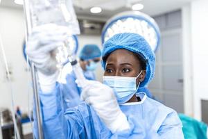 doctora afroamericana en el quirófano poniendo medicamentos a través de una iv - conceptos de cirugía