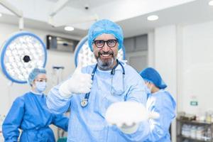 Plastic, Cosmetic Surgeon holding silicone breast implant and showing thumb up. Breast Augmentation Transplant. photo