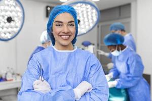 Portrait of female woman nurse surgeon OR staff member dressed in surgical scrubs gown mask and hair net in hospital operating room theater making eye contact smiling pleased happy looking at camera photo