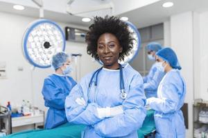 cintura arriba retrato de una trabajadora médica afroamericana con máscara protectora preparándose para la cirugía. cirujano y su asistente en un fondo borroso foto