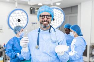 Mature Plastic surgeon man holding silicon breast implants in surgery room interior. Cosmetic surgery concept photo