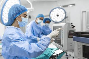 Anesthesiologist keeping track of vital functions of the body during cardiac surgery. Surgeon looking at medical monitor during surgery. Doctor checking monitor for patient health status. photo