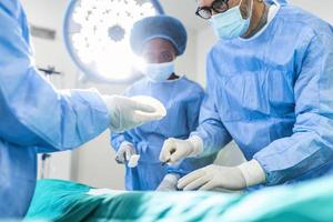 cirujano y su asistente realizando cirugía estética en el quirófano del hospital. cirujano enmascarado durante el procedimiento médico. aumento de senos, agrandamiento, realce foto