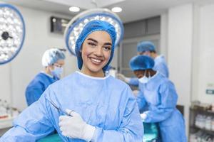 Portrait of female woman nurse surgeon OR staff member dressed in surgical scrubs gown mask and hair net in hospital operating room theater making eye contact smiling pleased happy looking at camera photo