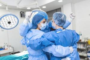 Partial view of hard-working male and female hospital team in full protective wear standing together in group embrace. photo