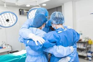 Partial view of hard-working male and female hospital team in full protective wear standing together in group embrace. photo