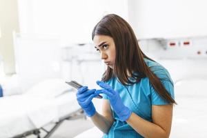 An exhausted female nurse sits on a bed in a hospital during a shift break. She daydreams while holding his smartphone. photo