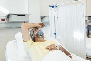 Male coronavirus patient looking away while resting on hospital bed. Man is wearing oxygen mask. He is in hospital during pandemic. photo