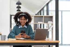 Photo of cheerful joyful mixed-race woman  playing games and wearing wireless headphones at home  Play game on your smartphone that wins the moment of victory. Fun and enjoyable vacation