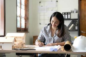 Architecture, building, construction and real estate concept - Happy smiling female architect with blueprint, ruler and living house model on table working at home office. Architect woman. photo