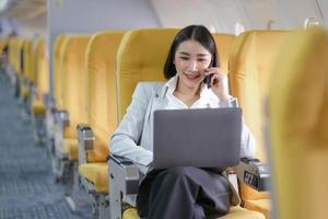 Asian woman passenger sitting in airplane near window and reading news from social networks or using travel applications in smartphone photo