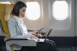 Asian woman passenger sitting in airplane near window and reading news from social networks or using travel applications in smartphone photo