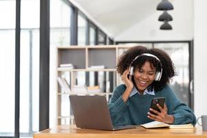 Photo of cheerful joyful mixed-race woman  playing games and wearing wireless headphones at home  Play game on your smartphone that wins the moment of victory. Fun and enjoyable vacation