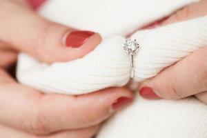 primer plano de un elegante anillo de diamantes de compromiso en el dedo de la mujer con ropa de invierno de suéter rosa. foto