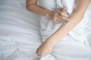 Asia woman sitting on bed and applying cream on her body. photo