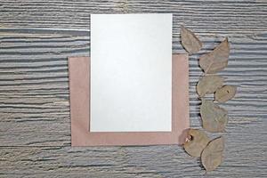 A5 paper greeting card mockup with dry leaves on wooden background photo