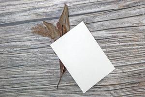 A5 paper greeting card mockup with dry leaves on wooden background photo