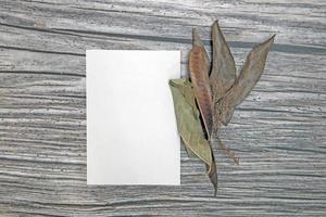 A5 paper greeting card mockup with dry leaves on wooden background photo