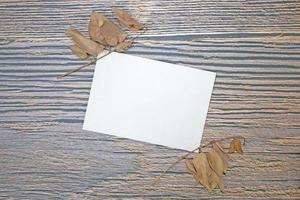 A5 paper greeting card mockup with dry leaves on wooden background photo