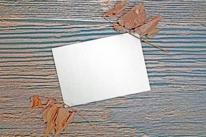 A5 paper greeting card mockup with dry leaves on wooden background photo