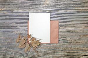 A5 paper greeting card mockup with dry leaves on wooden background photo