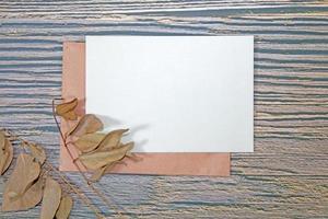 A5 paper greeting card mockup with dry leaves on wooden background photo