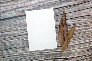 A5 paper greeting card mockup with dry leaves on wooden background photo