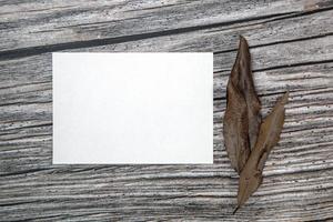 A5 paper greeting card mockup with dry leaves on wooden background photo