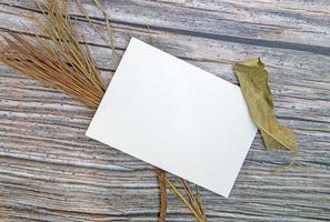 A5 paper greeting card mockup with dry leaves on wooden background photo