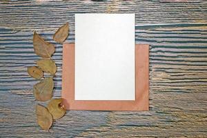 A5 paper greeting card mockup with dry leaves on wooden background photo