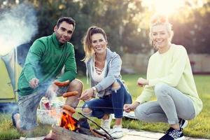 Group of friends preparing sausages on campfire photo