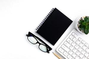 top view of modern white office desk with computer keyboard, blank notebook page and other equipment on white background. Workspace concept, workspace management style, business design space with copy photo