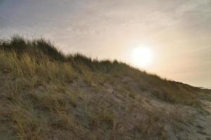 cruce de playa en dinamarca por el mar. dunas, agua de arena y nubes en la costa. foto